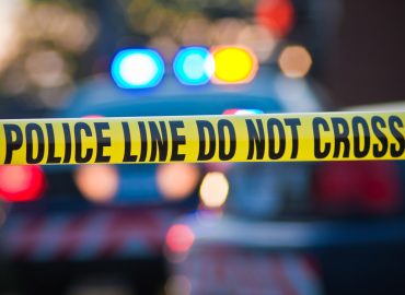 Shallow depth of field image taken of yellow law enforcement line with police car and lights in the background.