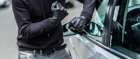 The man dressed in black with a balaclava on his head trying to break into the car. He uses a screwdriver. Car thief, car theft concept